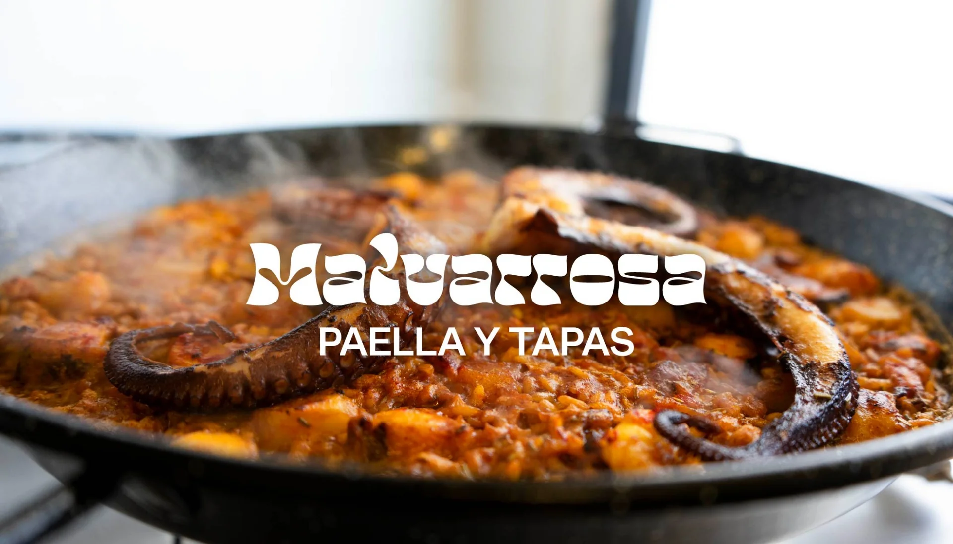 Malvarrosa Paella y Tapas: logo bianco su una fotografia della paella